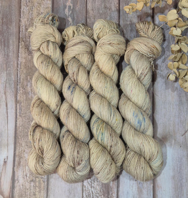 Four skeins of beige yarn on a wooden surface with dried flowers.